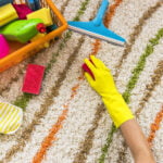 Hand with gloves on cleaning a carpet with toys