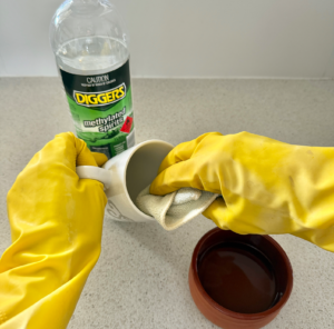 Removing coffee stains from a ceramic mug using DIGGERS Methylated Spirits and a cloth with rubber gloves